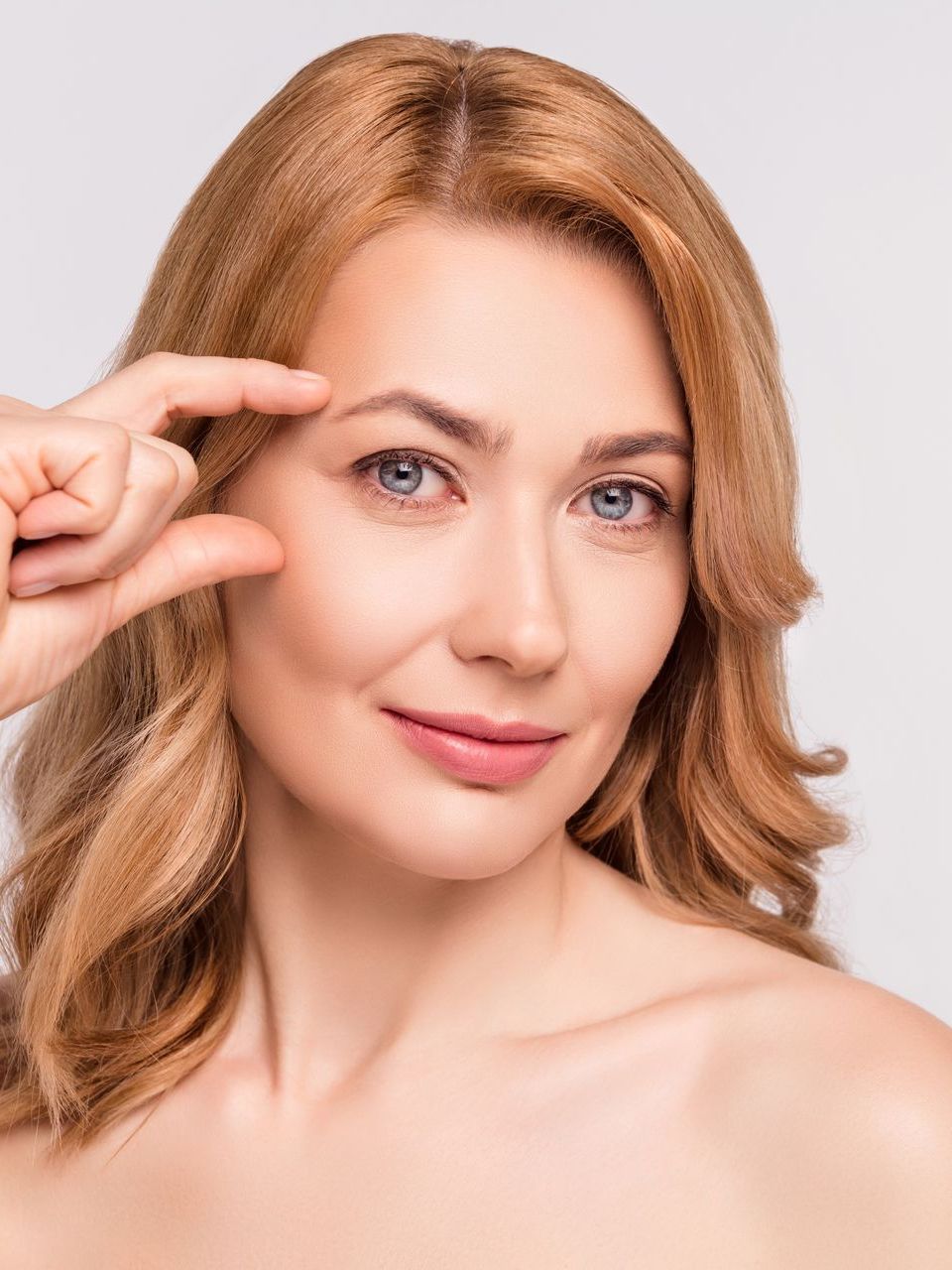 A woman is touching her eyebrow with her finger.