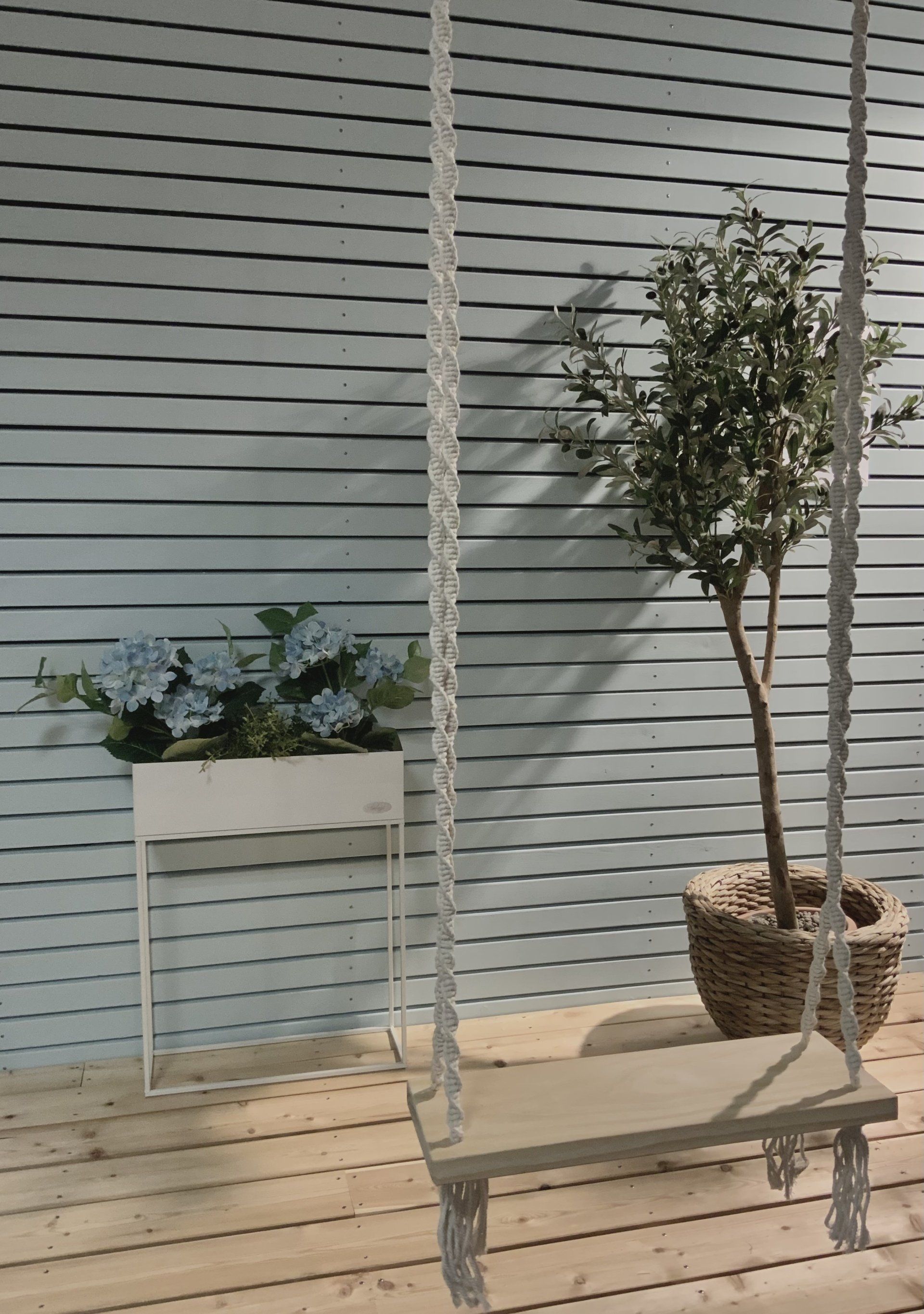 Ein Baum in einem Topf steht auf einem Holzdeck neben einer Schaukel.