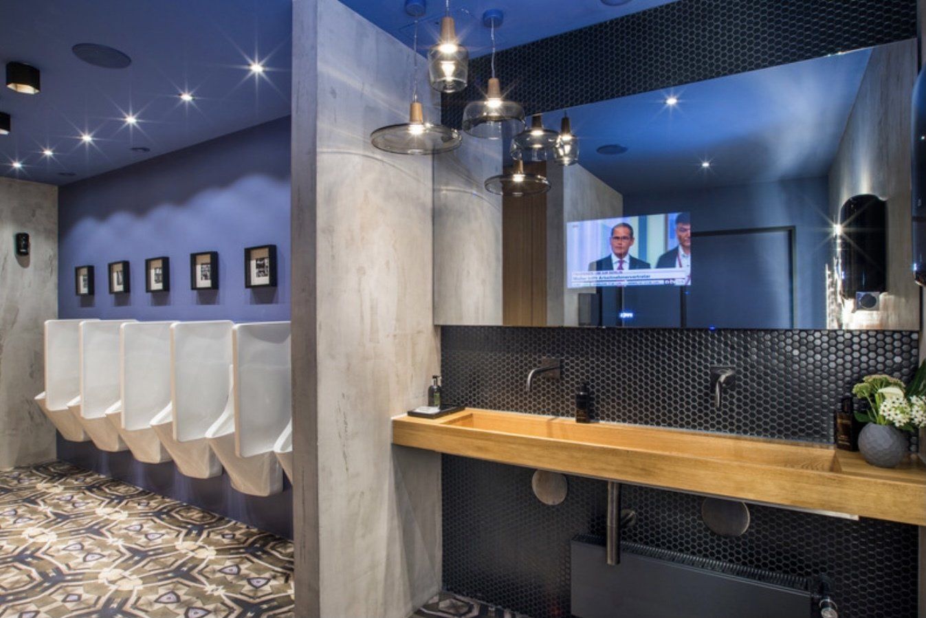 Ein Badezimmer mit Urinalen und Waschbecken und einem Fernseher an der Wand.