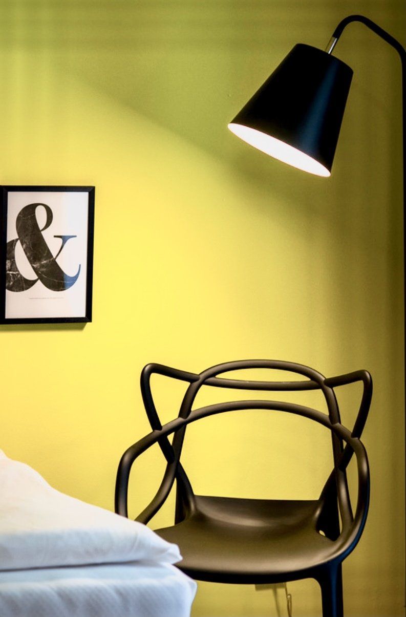 Ein schwarzer Stuhl steht vor einer gelben Wand neben einer Lampe