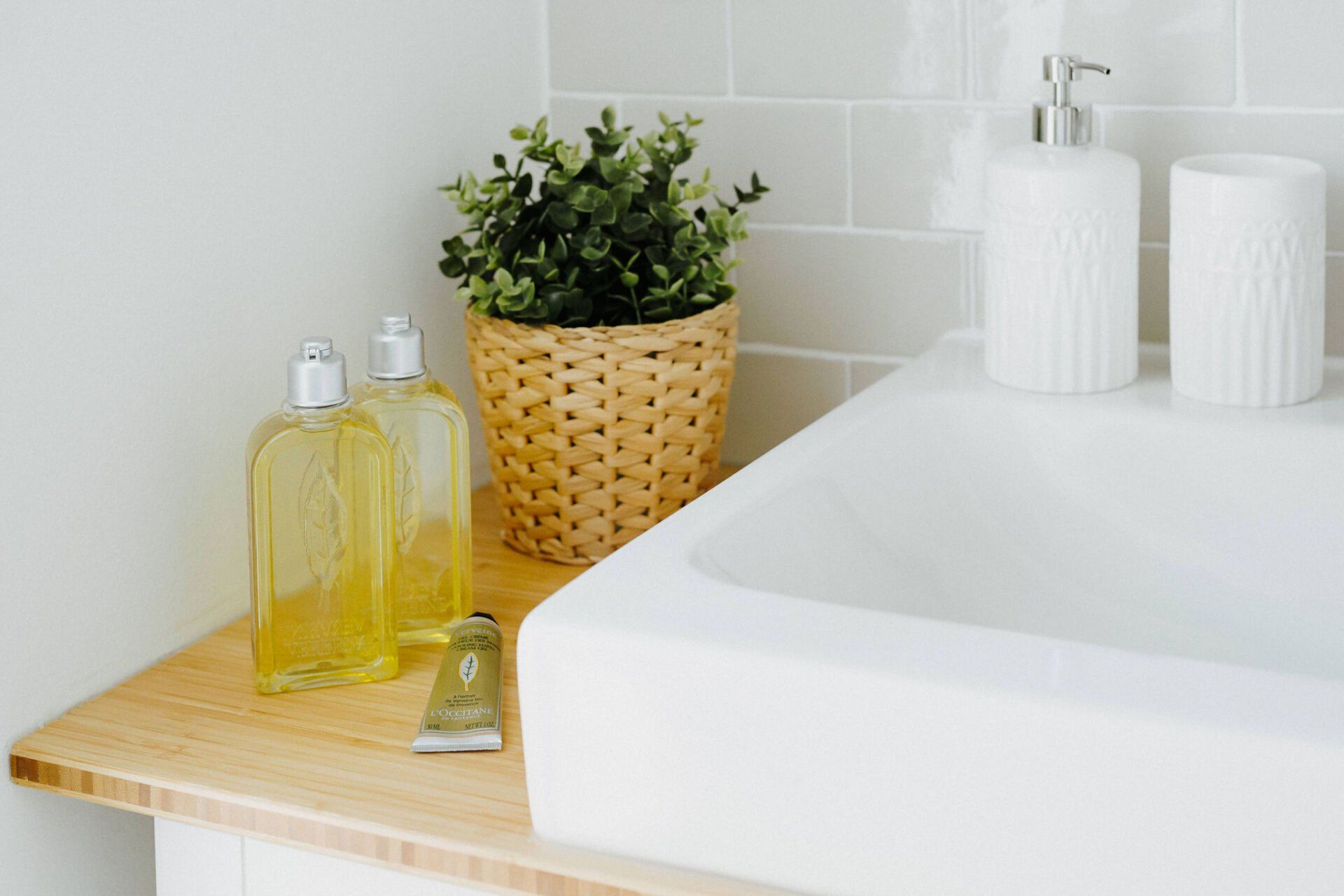 Ein Waschbecken im Badezimmer mit zwei Flaschen Seife und einer Pflanze in einem Korb.
