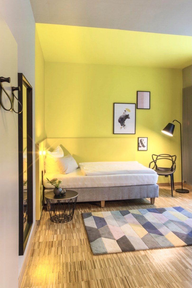Ein Schlafzimmer mit gelben Wänden, einem Bett, einem Teppich, einem Spiegel und einer Lampe.