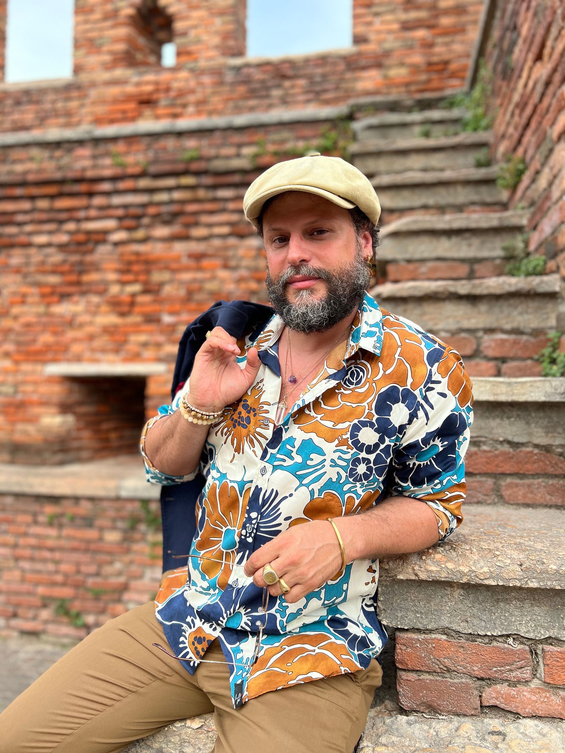 Ein Mann mit Bart sitzt auf einer Treppe vor einer Backsteinmauer.