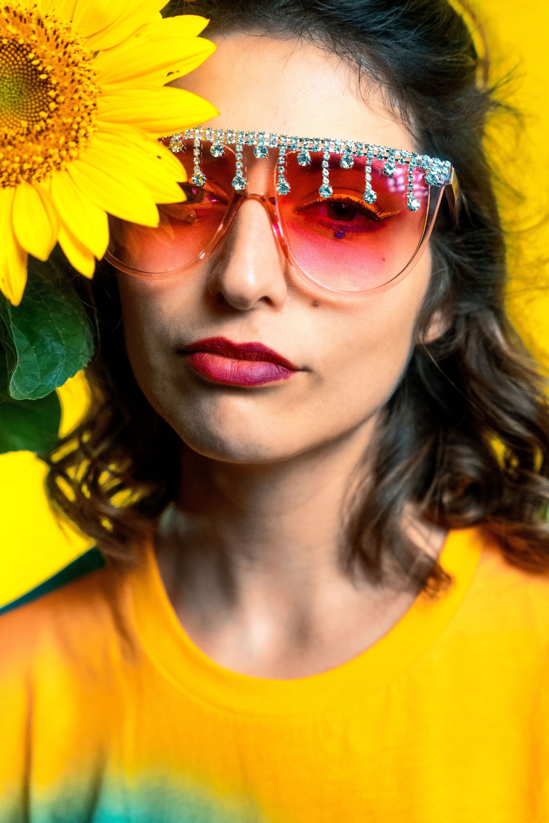 Eine Frau mit Sonnenbrille hält eine Sonnenblume vor ihr Gesicht.