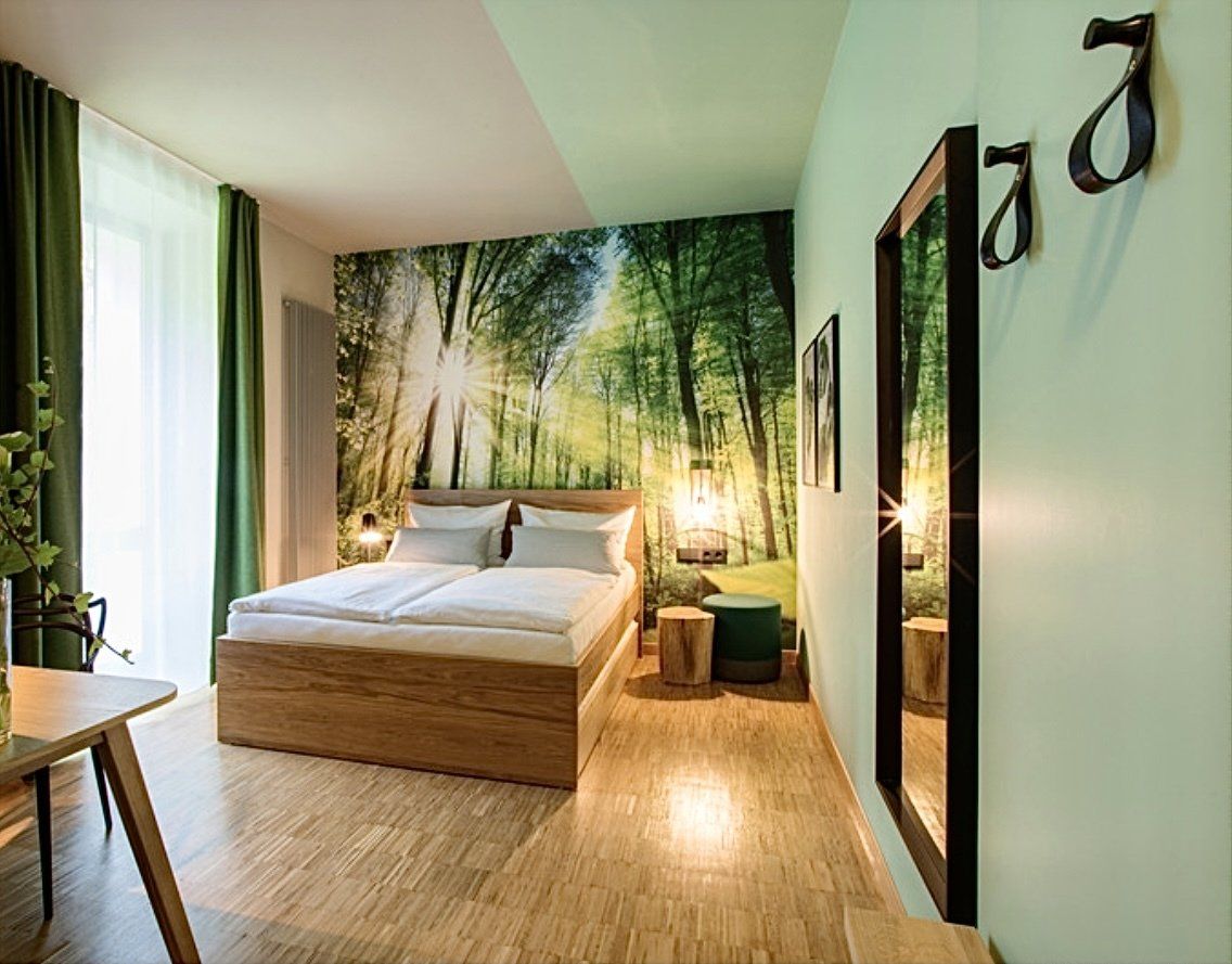 Ein Hotelzimmer mit Bett, Tisch, Spiegel und Wandgemälde an der Wand.