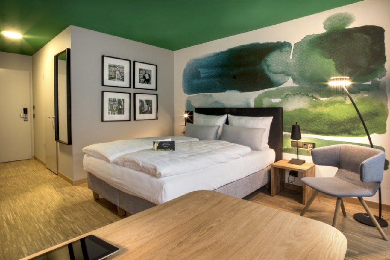 Ein Hotelzimmer mit Bett, Schreibtisch, Stuhl und einem Gemälde an der Wand.