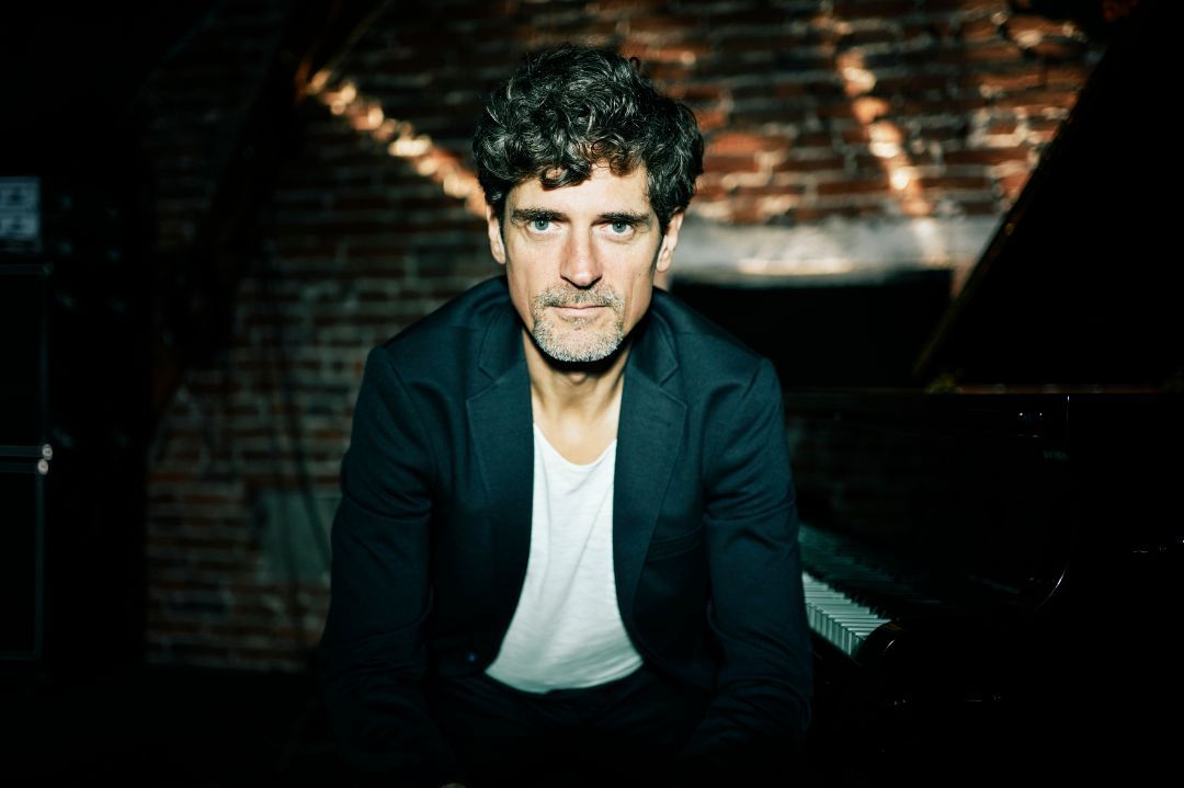 Ein Mann in Anzug und weißem Hemd sitzt vor einem Klavier.