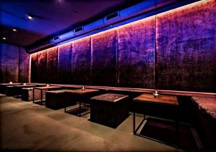 Eine Reihe von Tischen und Stühlen in einem dunklen Raum mit violetten Lichtern an der Wand.