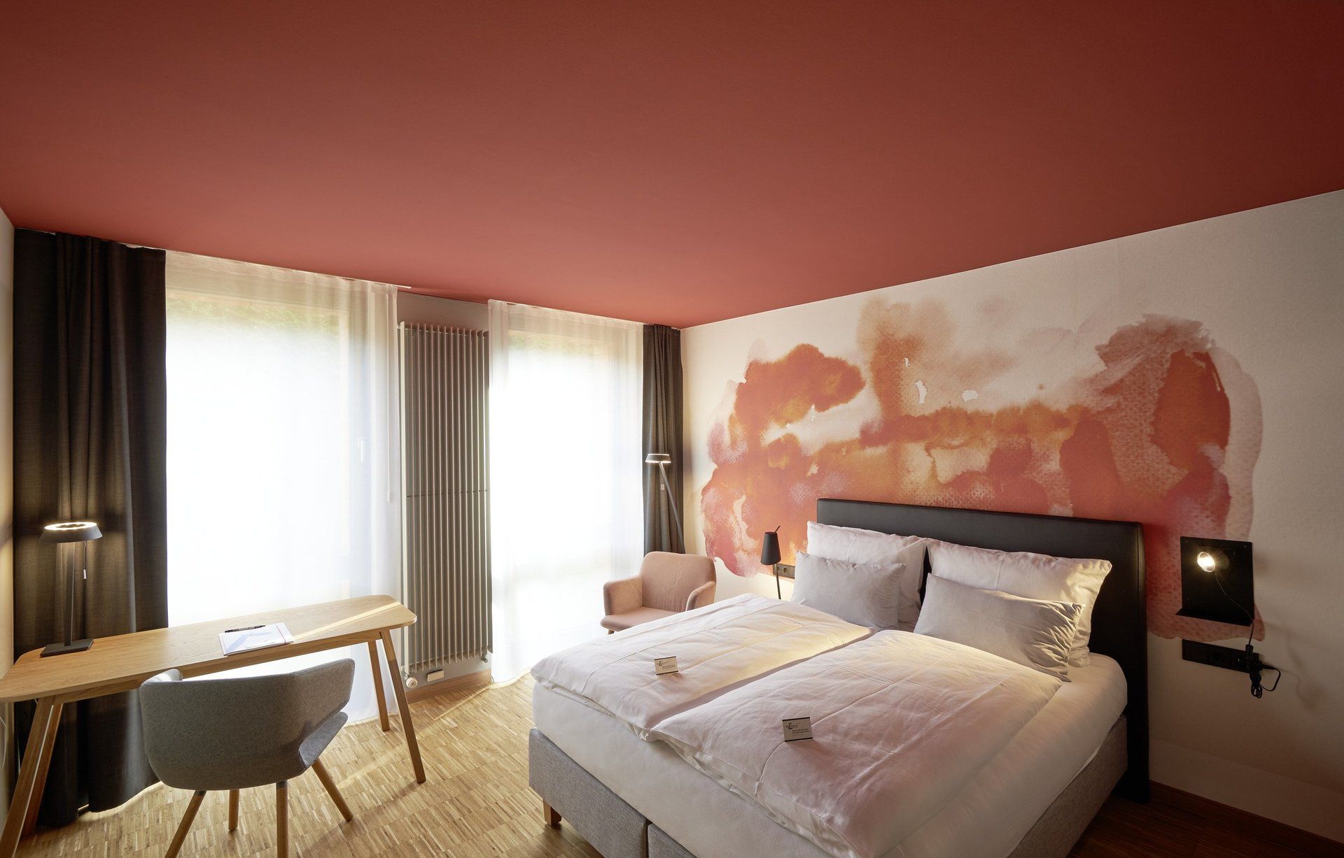 Ein Hotelzimmer mit Bett, Schreibtisch, Stuhl und Fenster.