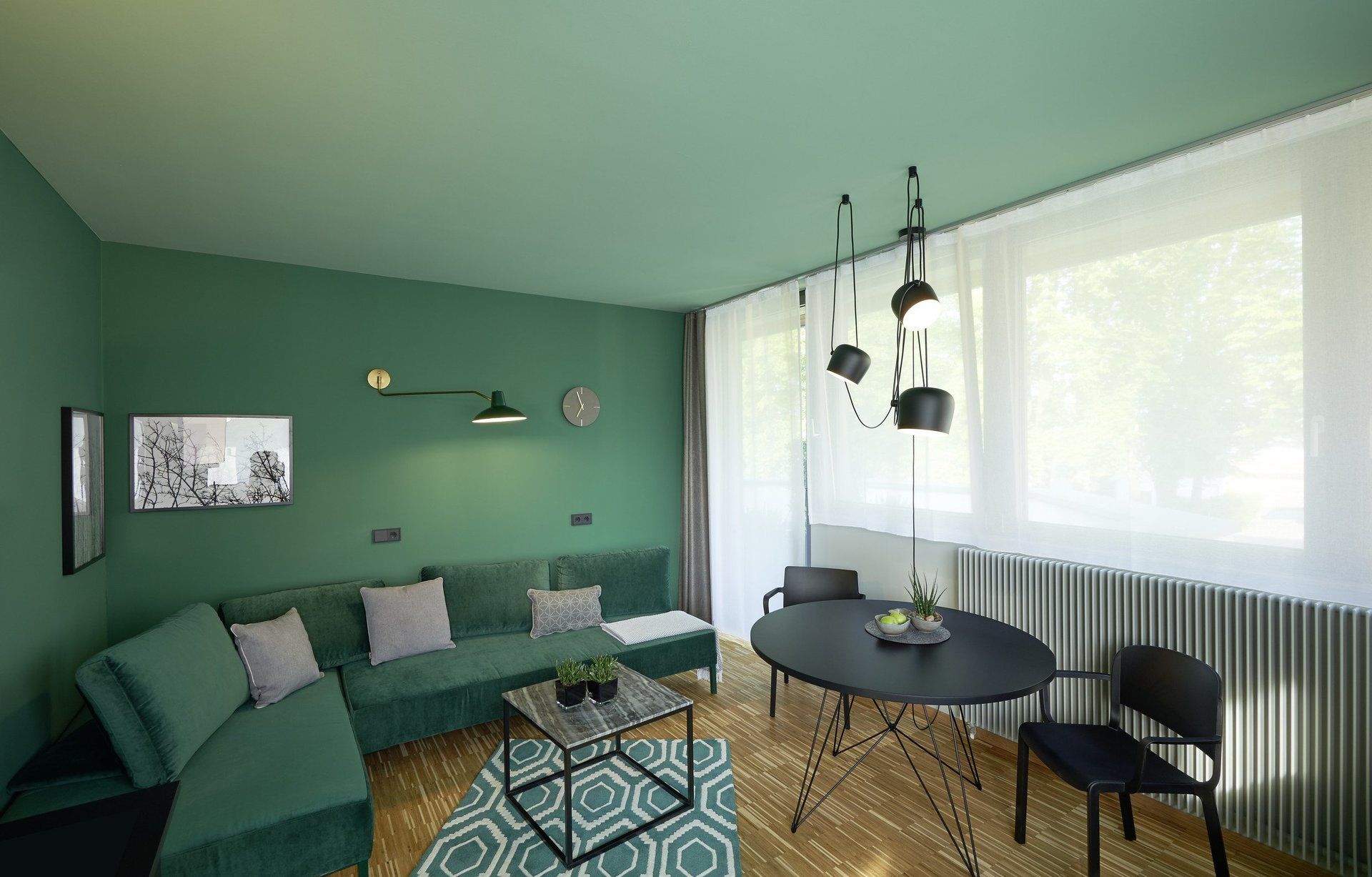 Ein Wohnzimmer mit grünen Wänden, einer grünen Couch, einem Tisch und Stühlen.