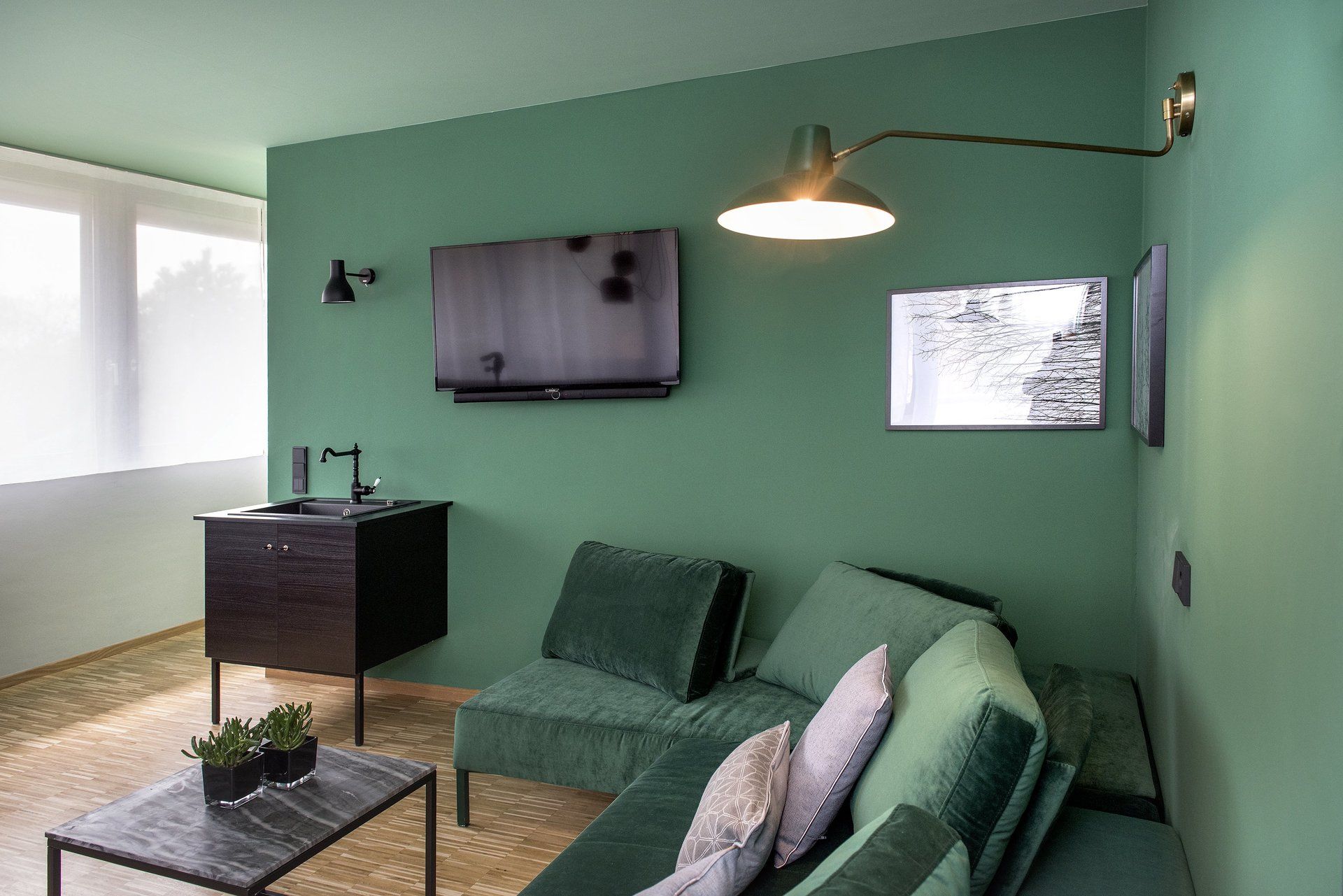 Ein Wohnzimmer mit grünen Wänden, einer grünen Couch, einem Couchtisch und einem Flachbildfernseher.