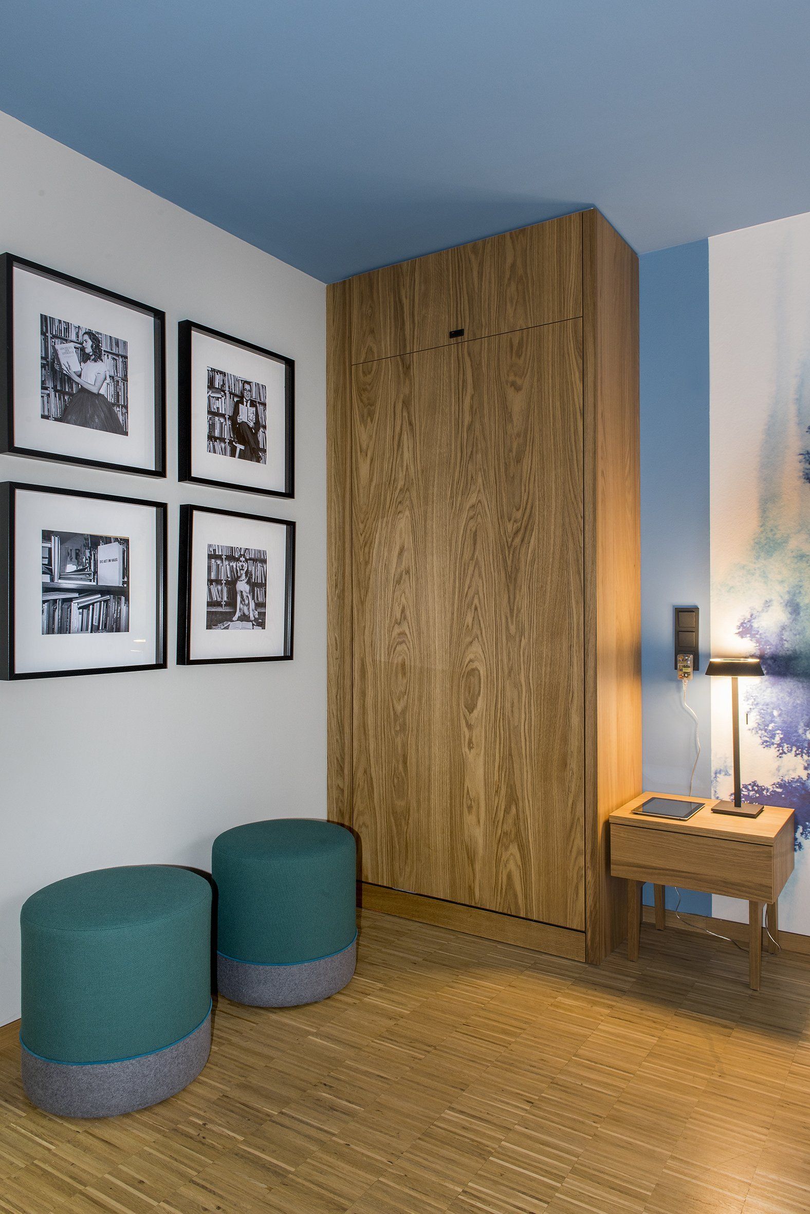 Ein Zimmer mit einem Holzschrank, zwei Ottomanen, einem Nachttisch und Bildern an der Wand.