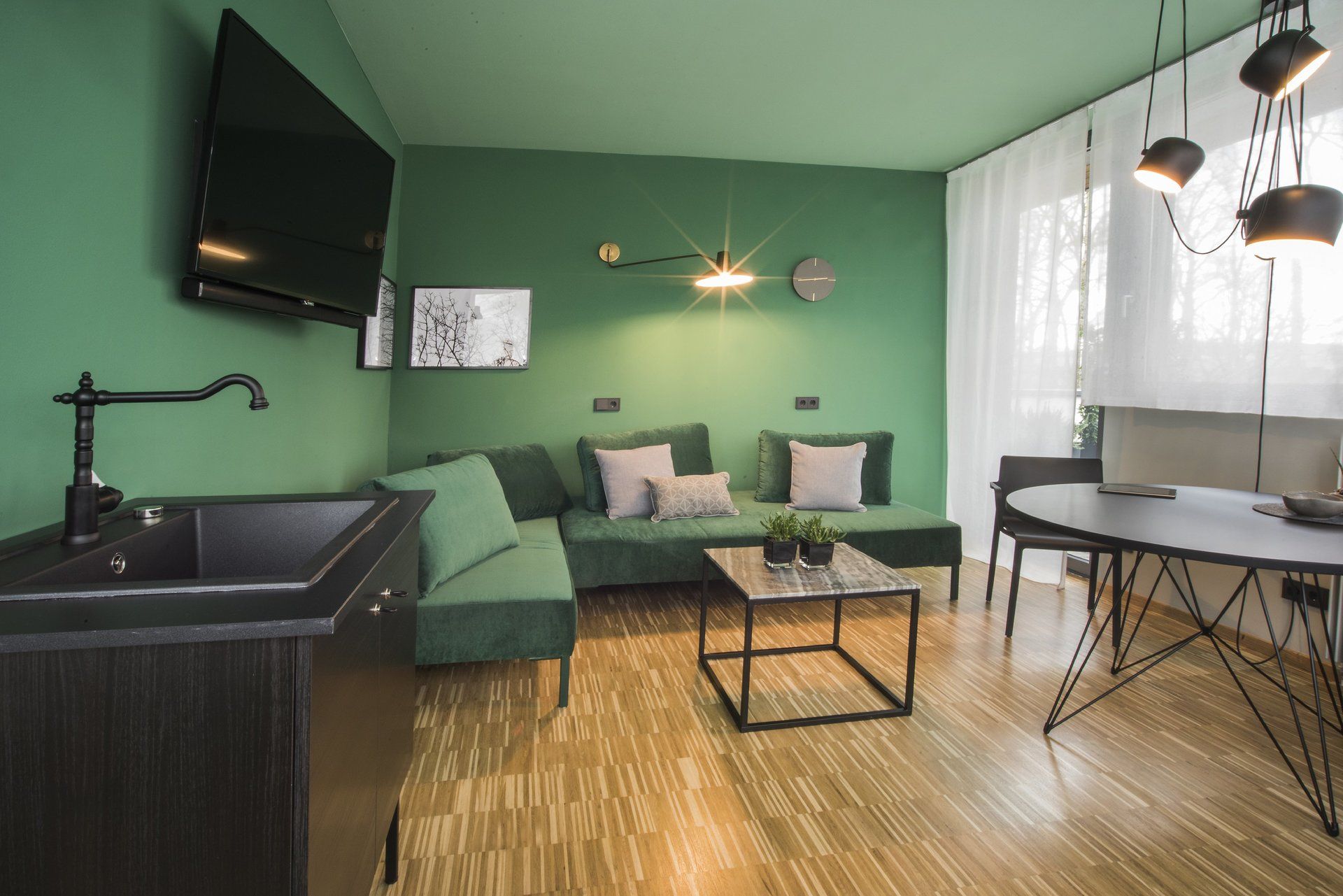 Ein Wohnzimmer mit grünen Wänden, einer Couch, einem Tisch, einem Waschbecken und einem Flachbildfernseher.
