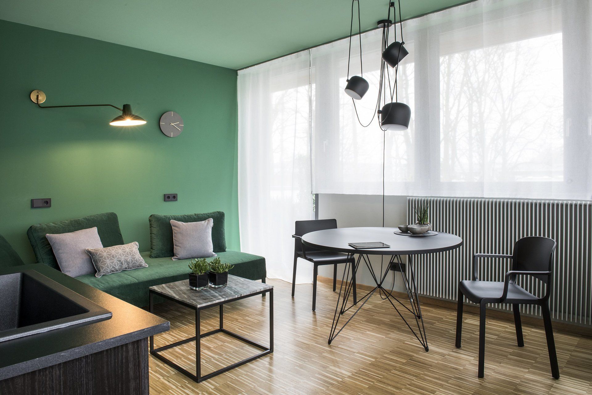 Ein Wohnzimmer mit grünen Wänden, einer Couch, einem Tisch und Stühlen.