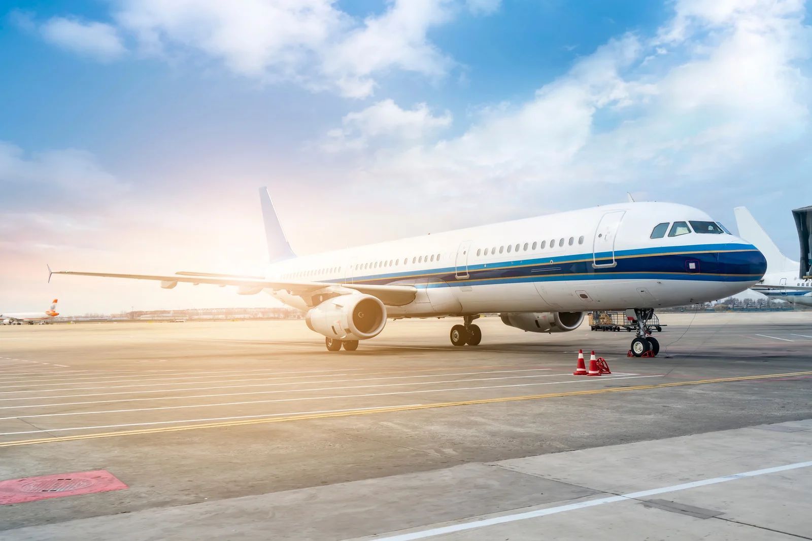 White and blue passenger airplane on tarmac under a blue, cloudy sky.