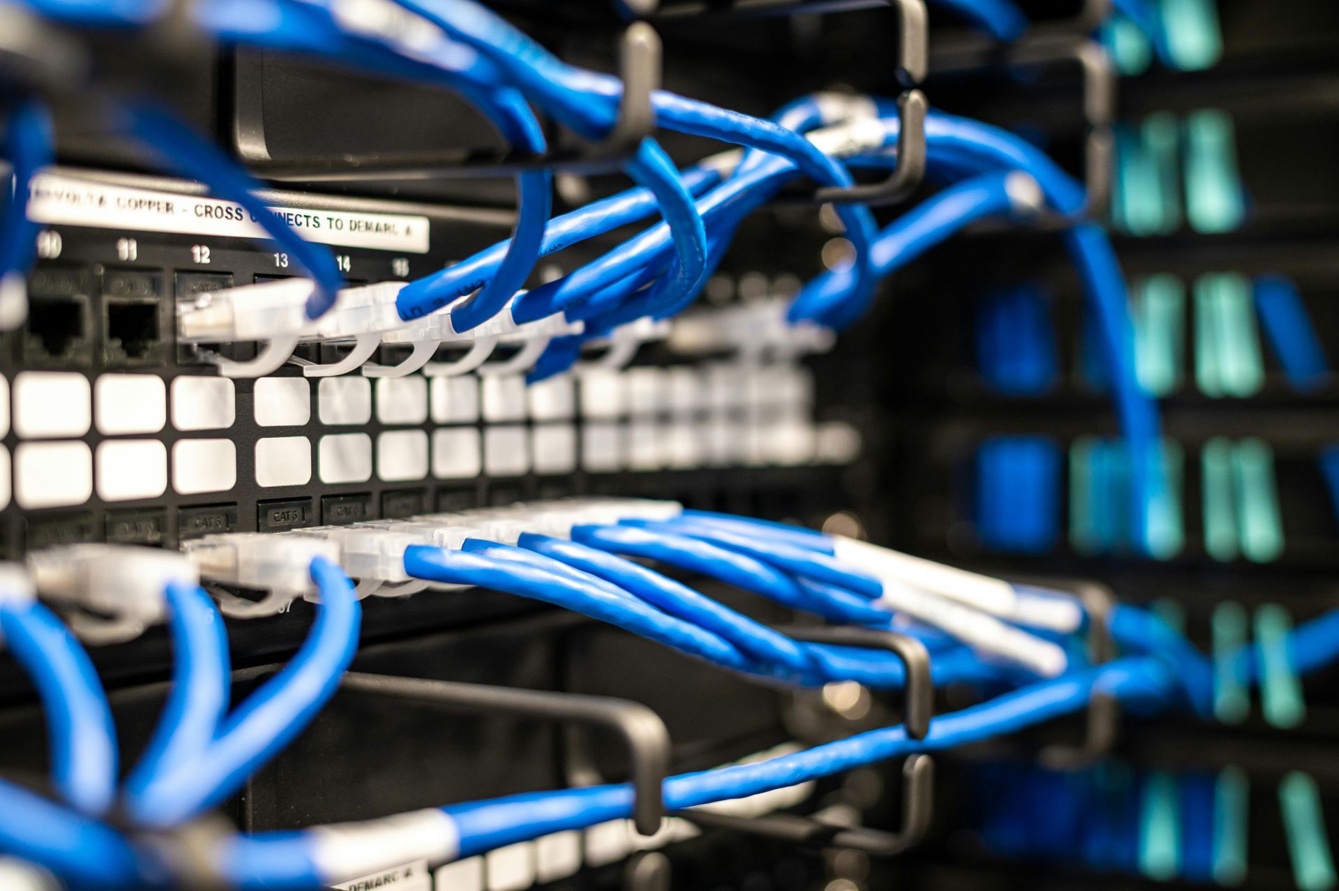 A bunch of blue wires are hanging from a rack in a server room.