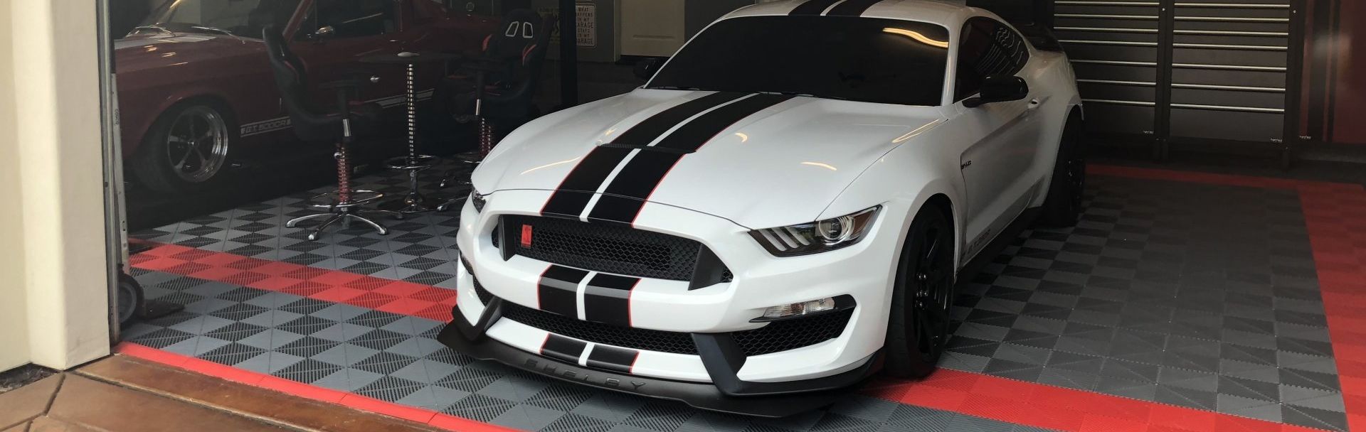 A white mustang with black stripes is parked in a garage.