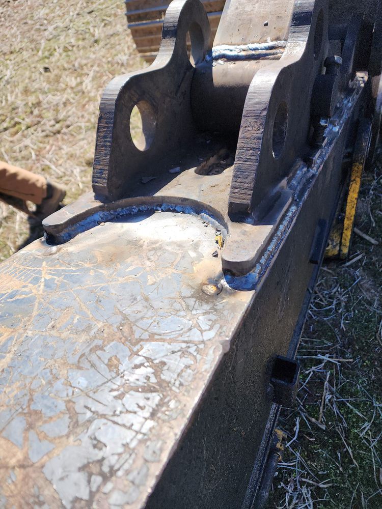 A person is welding a piece of metal in the grass.