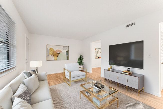 Living room with white walls, couch, armchair, TV, coffee table, and artwork.