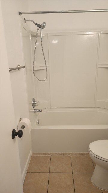 Bathroom with white tub and shower, toilet, and beige tile floor.