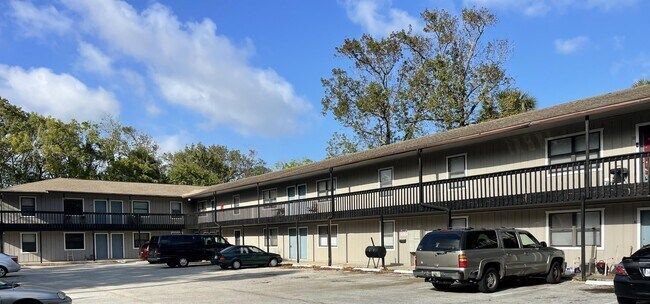 Apartment building exterior with parked vehicles under a blue sky with scattered clouds.