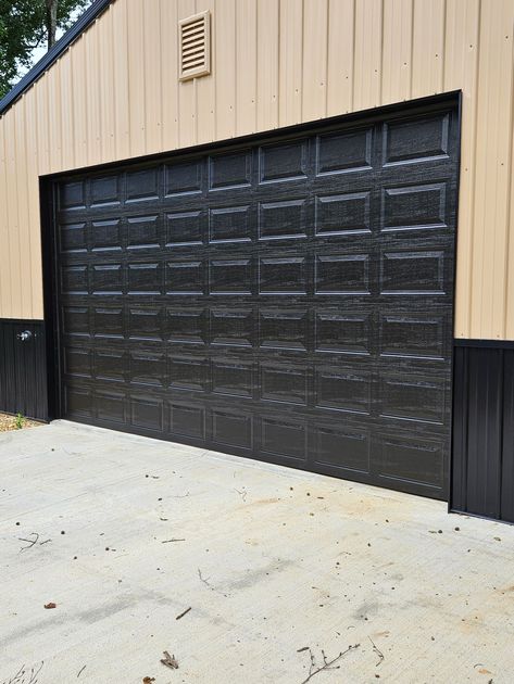 A black garage door is sitting on the side of a building.