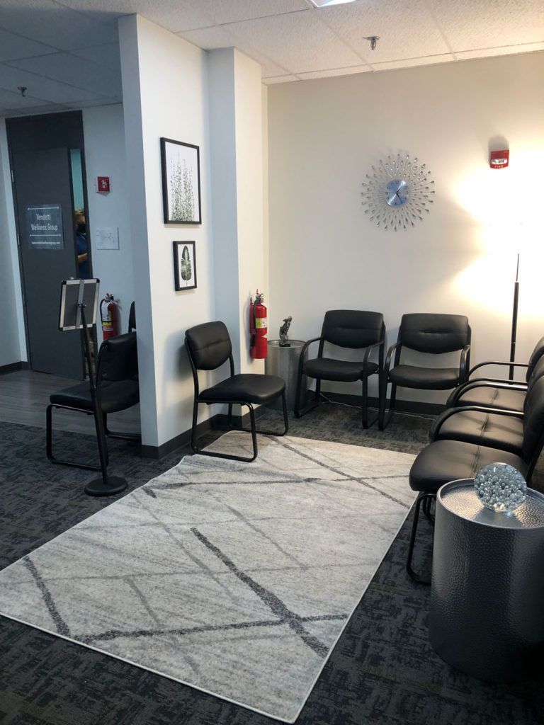 A waiting room with chairs , a rug and a clock on the wall.
