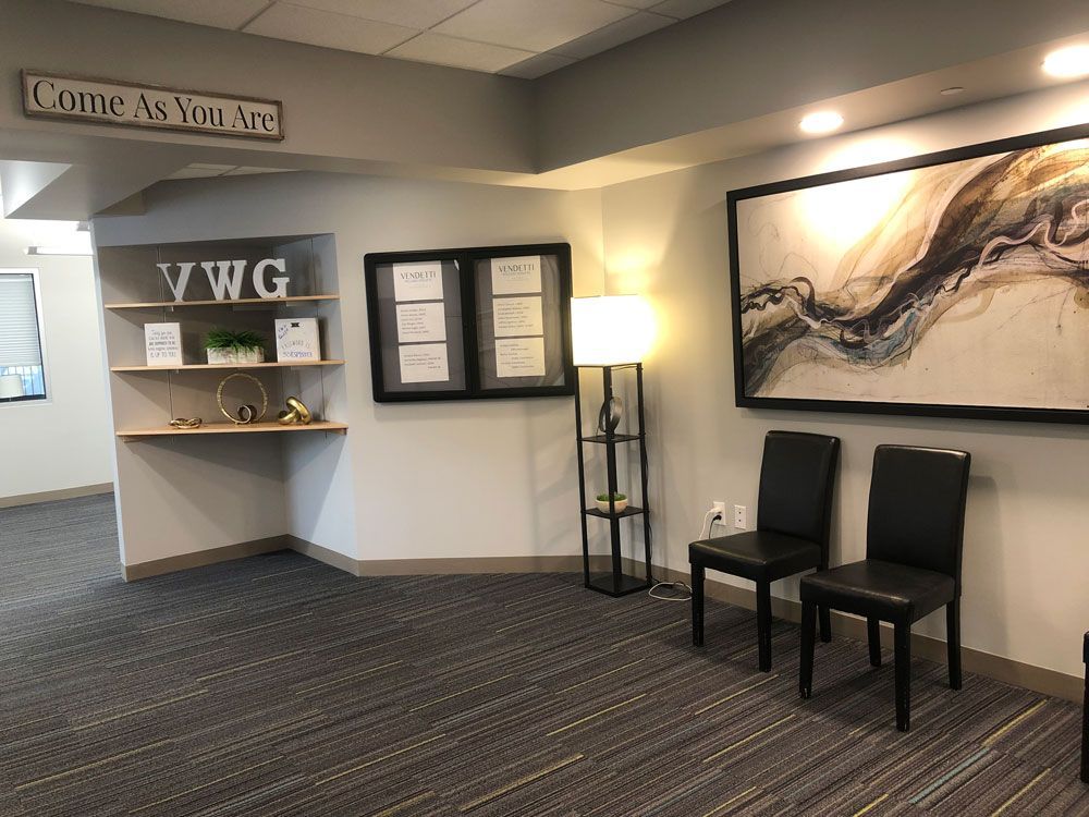 A waiting room with two chairs , a lamp and a painting on the wall.
