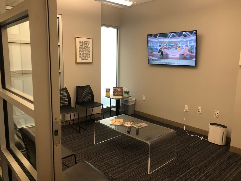 A waiting room with a table and chairs and a flat screen tv on the wall.