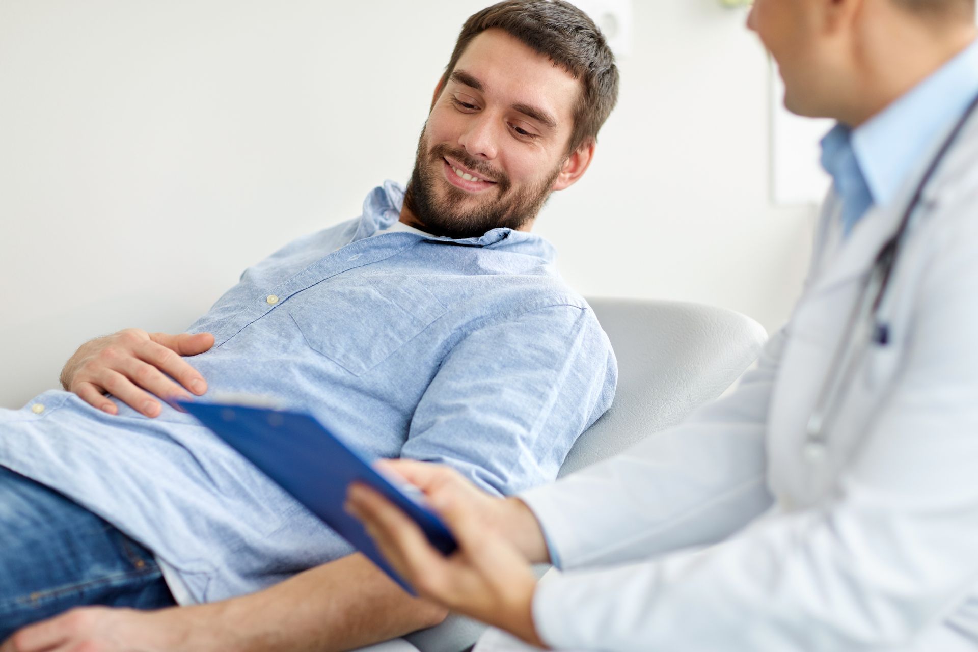 A man is sitting in a chair talking to a doctor while holding a clipboard.