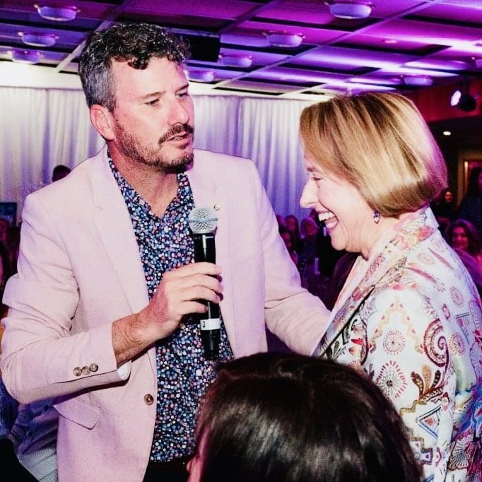 clayton menyweather in a pink jacket is holding a microphone and talking to a woman