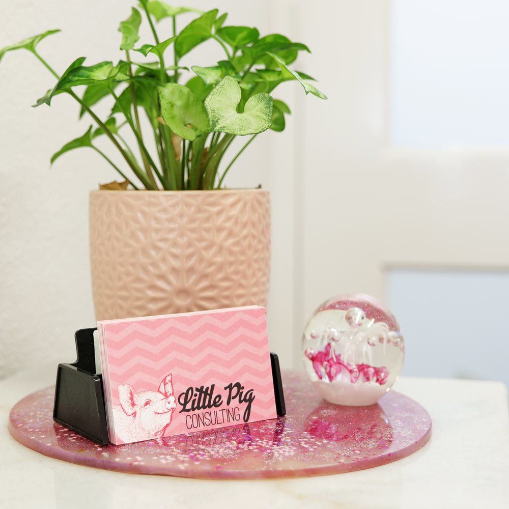 A business card for little pig consulting sits on a table next to a potted plant