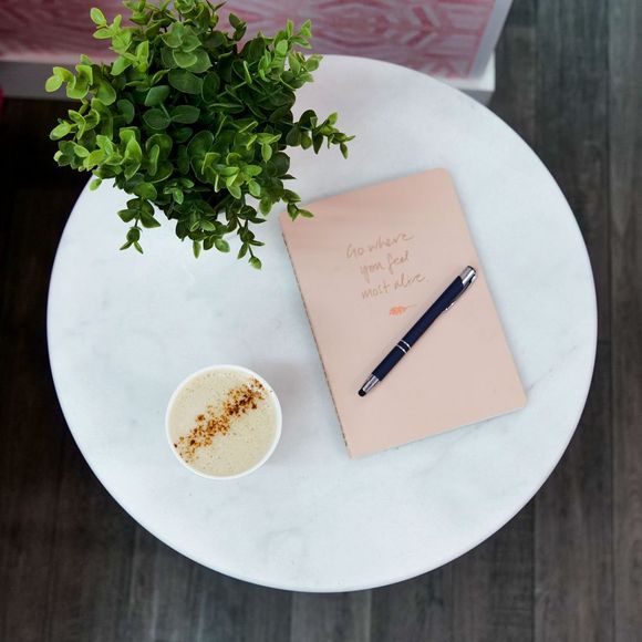 A notebook with a pen and a cup of coffee on a table