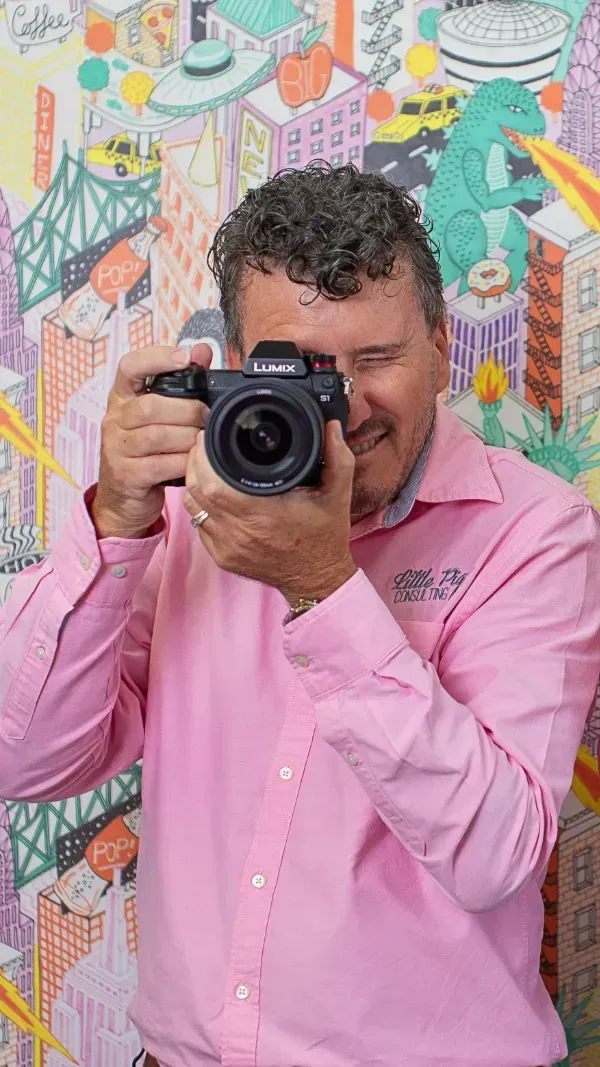 Clayton Menyweather in a pink shirt taking a picture with a camera.