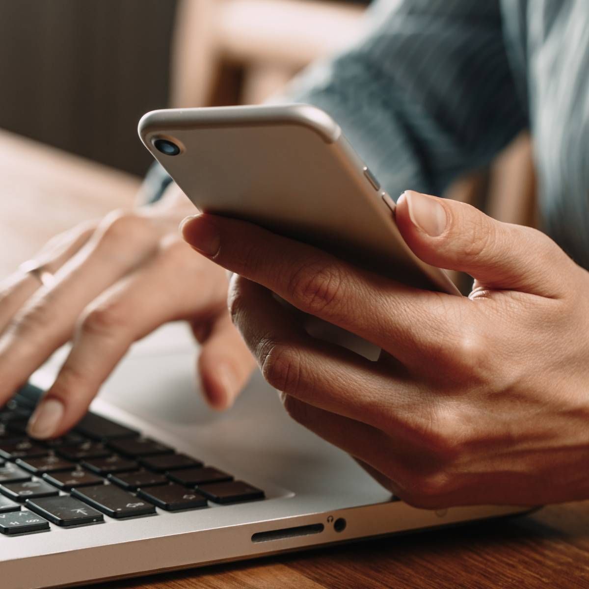 Person using a laptop with one hand while holding a smartphone in the other hand.