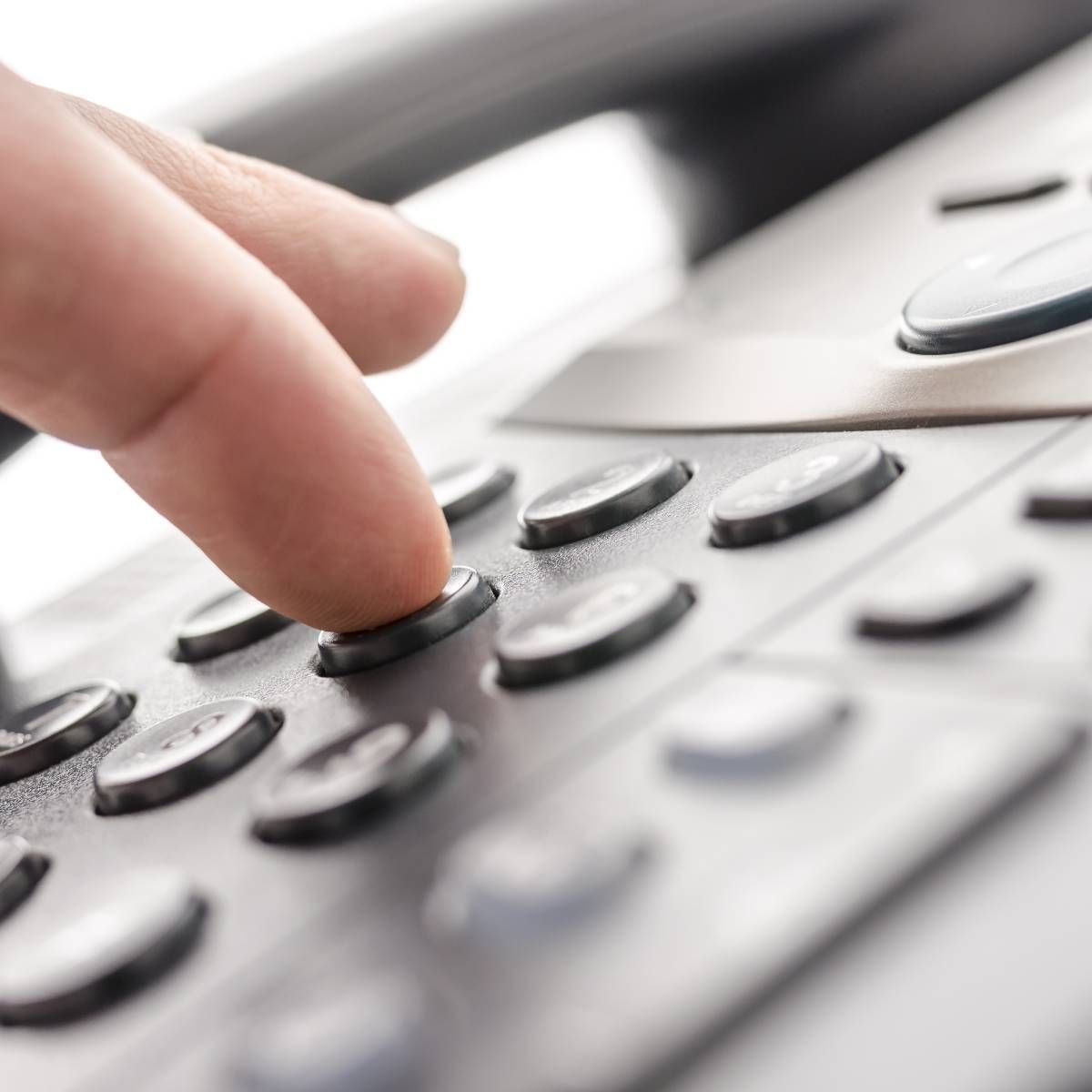 Finger pressing a button on a grey office phone keypad.