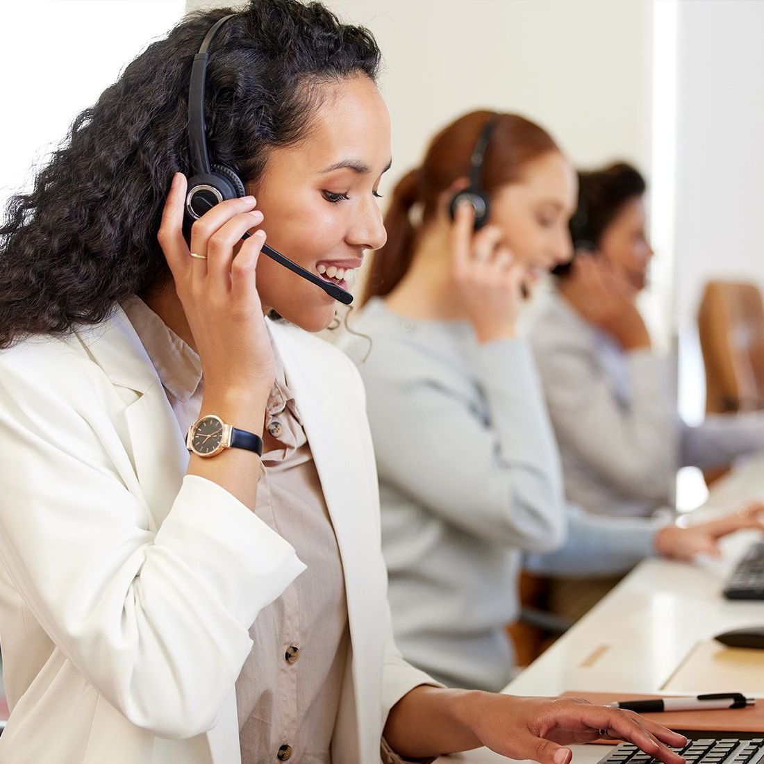 A woman wearing a headset is smiling while typing on a laptop