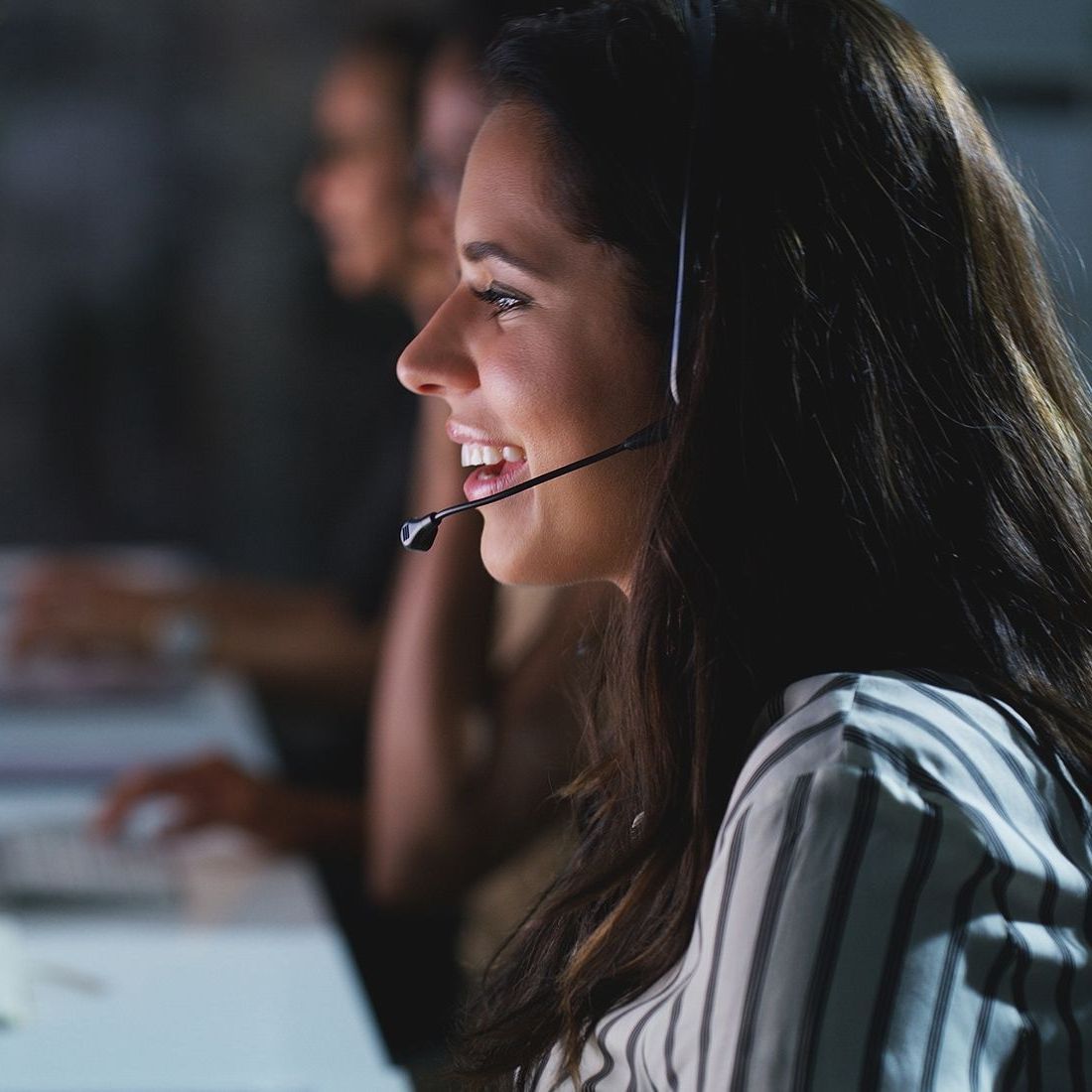 A woman wearing a headset is smiling while using a computer.