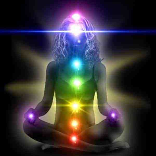 A woman is sitting in a lotus position with a rainbow of chakras surrounding her.