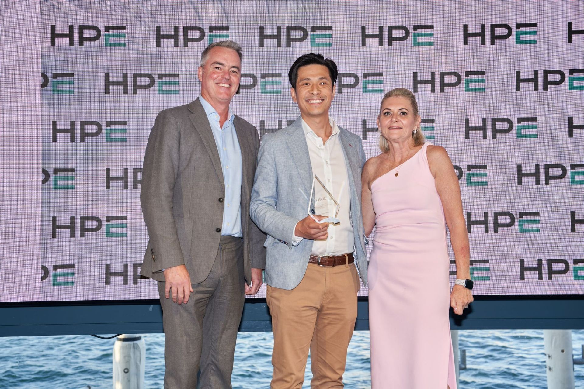 Three people posing for a photo at an HPE event, with an award. Background has HPE logos.