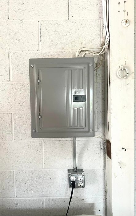 A gray electrical box is hanging on a white brick wall.