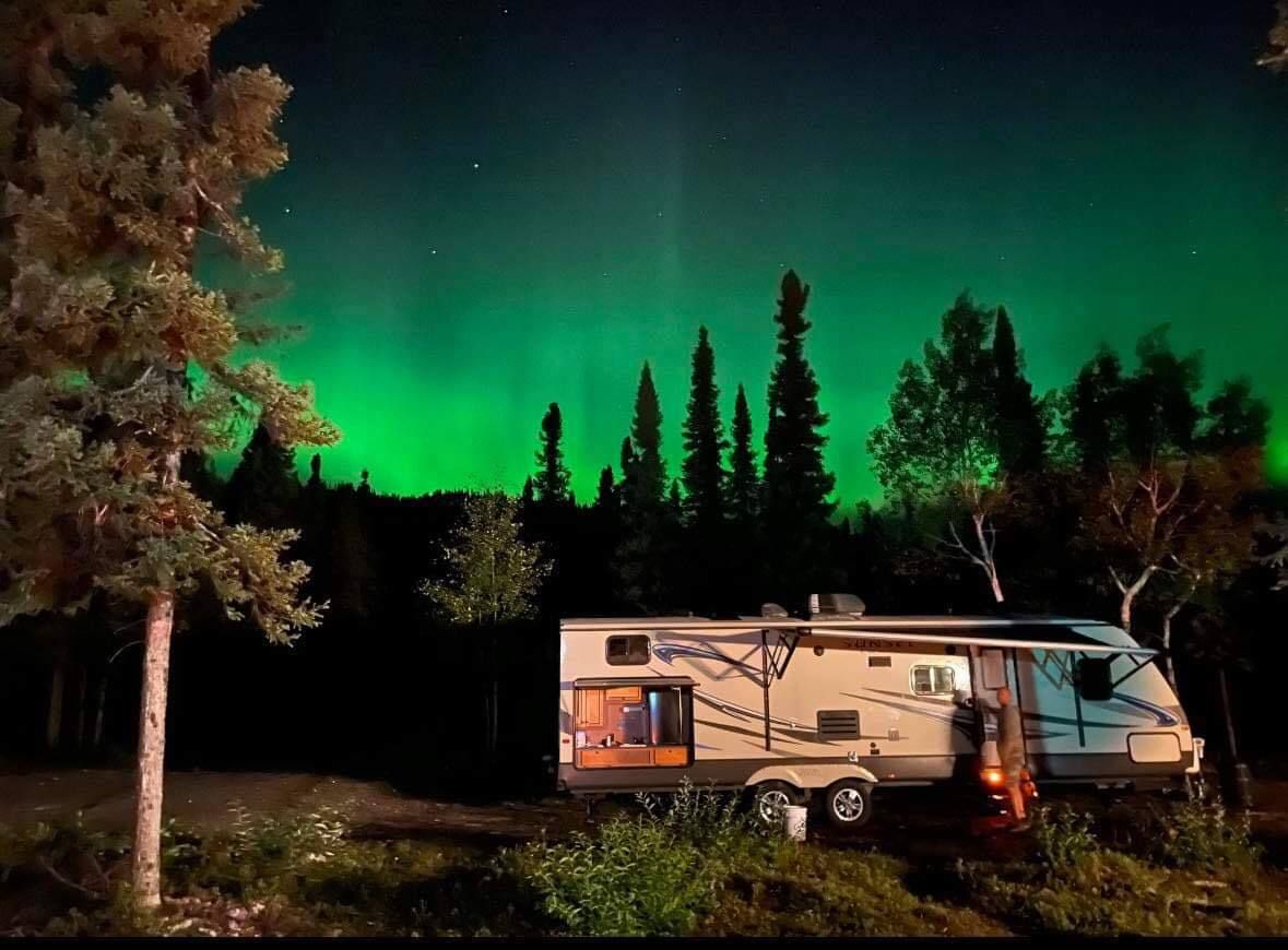 A rv is parked in the woods under the aurora borealis