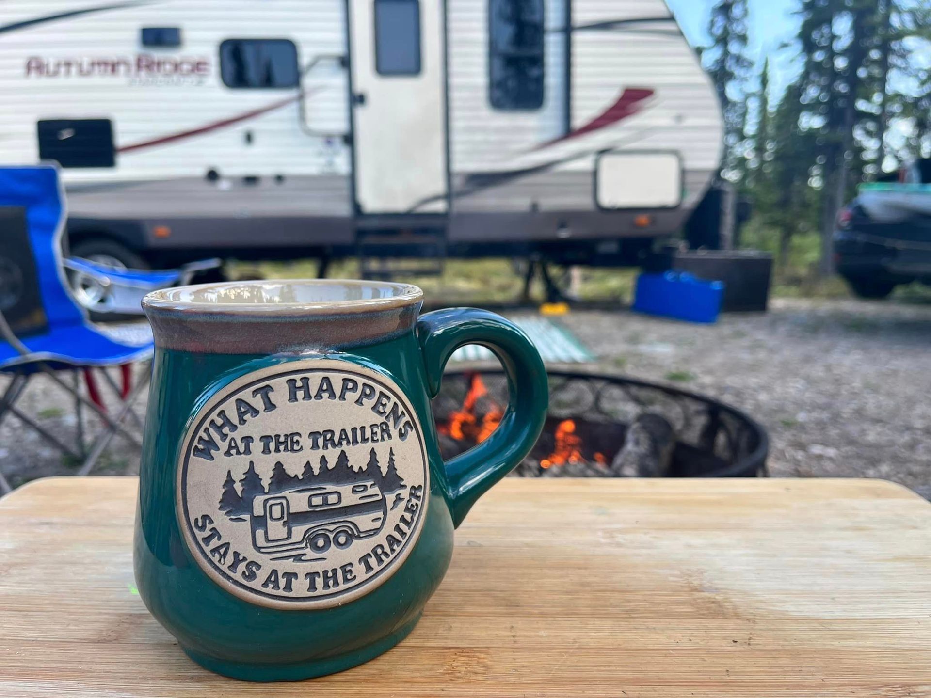 A green mug that says `` what happens at the trailer stays at the trailer '' is sitting on a wooden table.