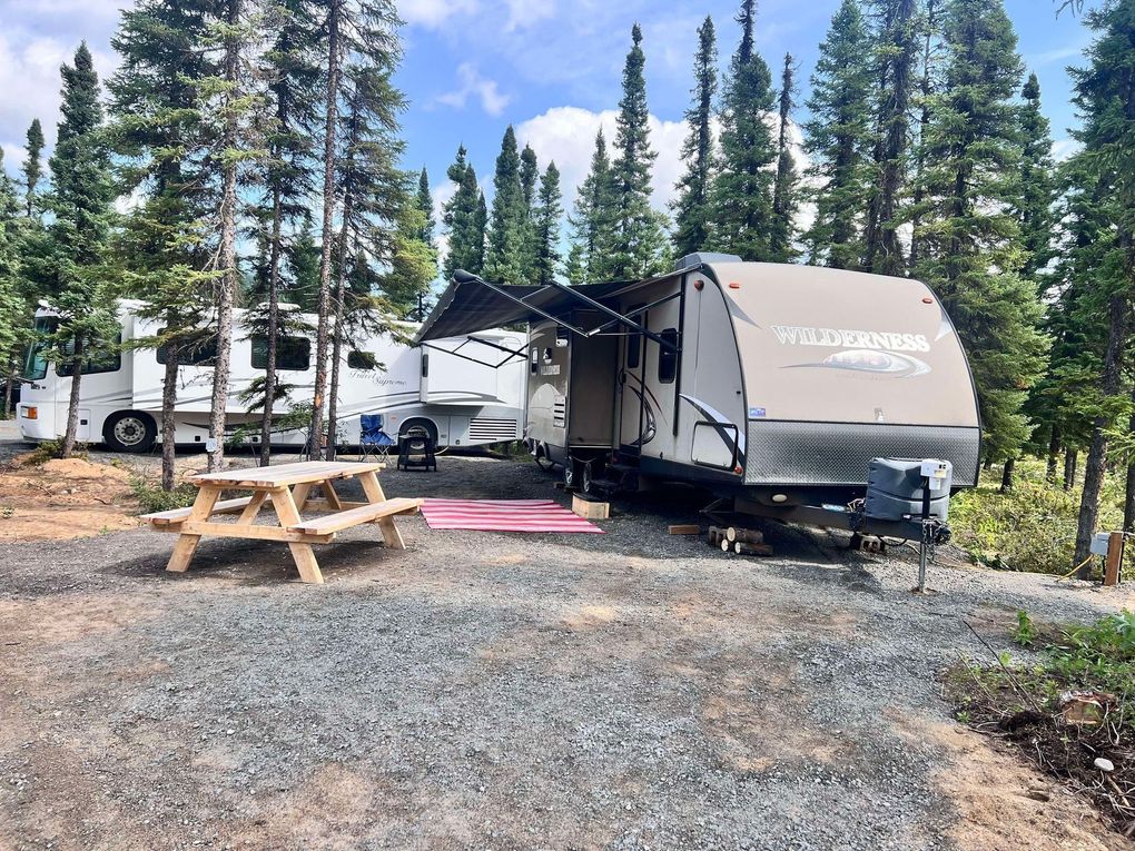 A rv is parked in a gravel lot with a picnic table.