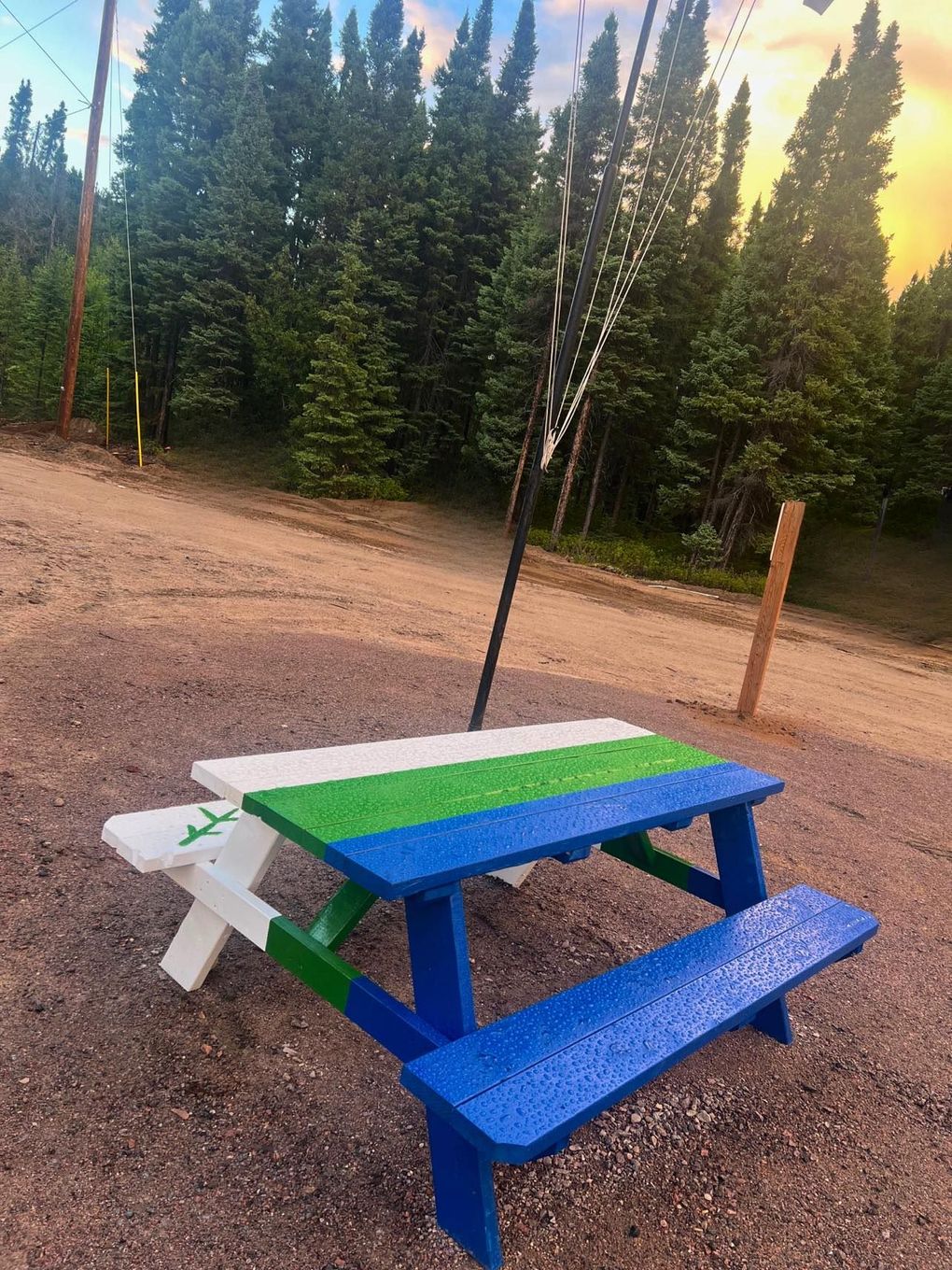 A blue , green and white picnic table is sitting on the side of a dirt road.