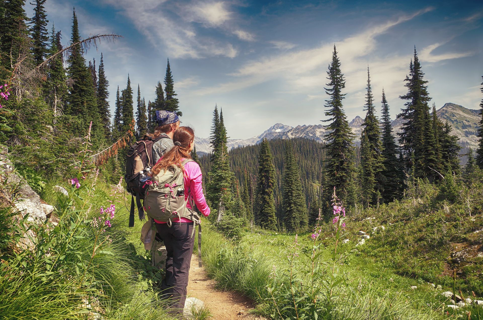 A man and a woman are hiking down a trail in the woods.