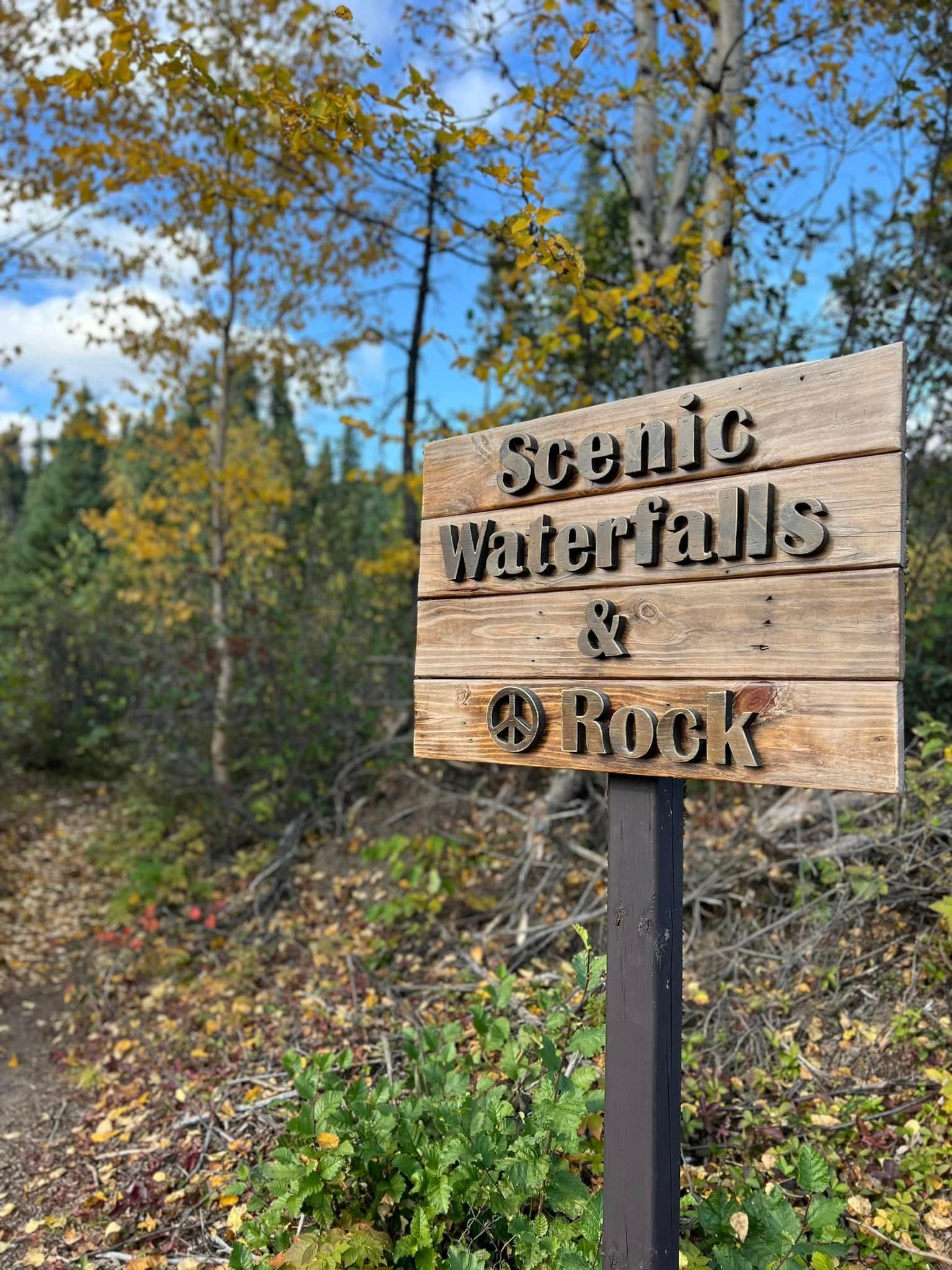 A wooden sign for scenic waterfalls and rocks in the woods.