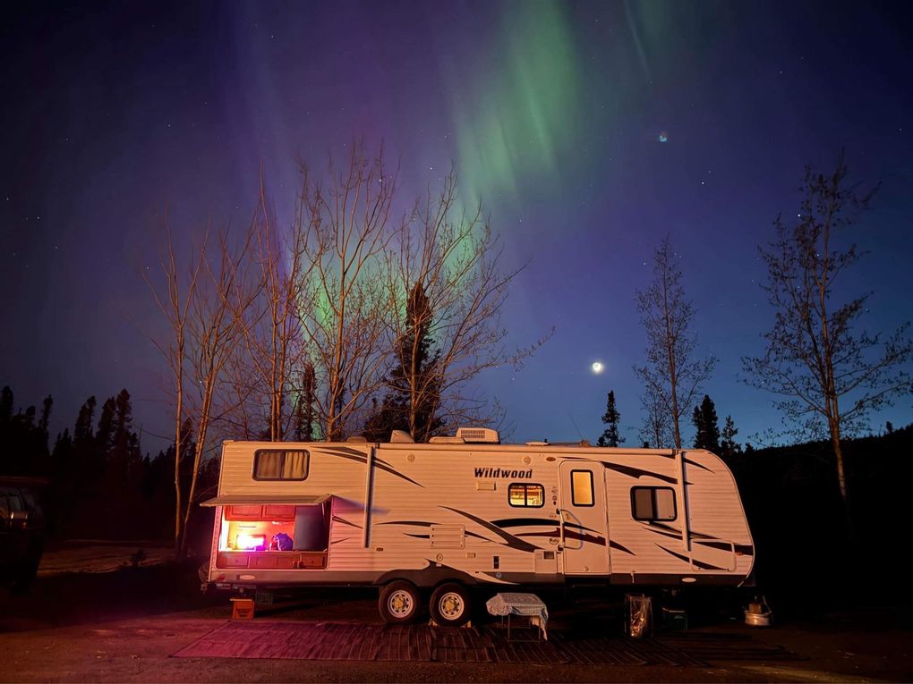 A rv is parked in front of the aurora borealis.