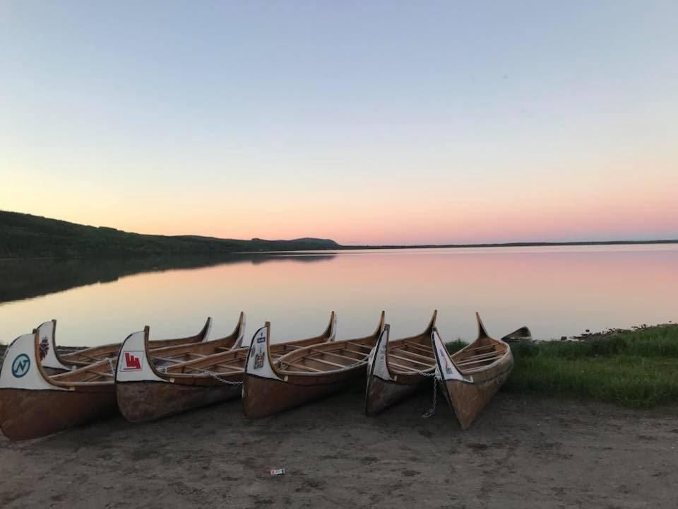 A row of canoes are lined up on the shore of a lake at sunset.