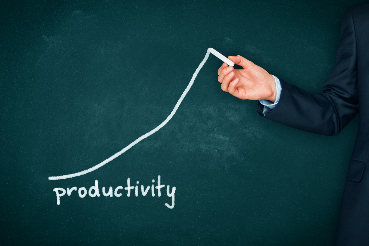 Person in a suit drawing an upward-trending productivity graph on a chalkboard.